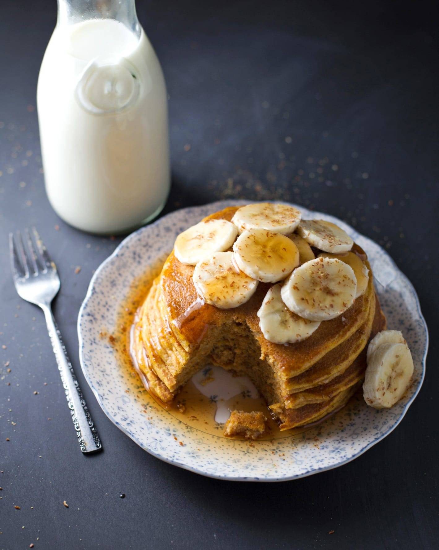 Stack of pancakes on a plate with milk.